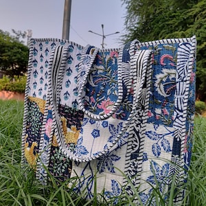 Könnte beinhalten: Eine Patchwork-Tragetasche mit blauen, weißen und schwarzen Blumenmustern. Die Tasche hat zwei schwarz-weiß gestreifte Henkel.