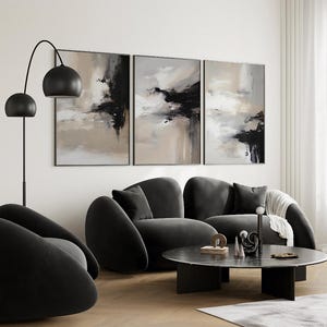 Könnte beinhalten: Ein modernes Wohnzimmer mit drei abstrakten Kunstwerken in neutralen Tönen. Eine schwarze Stehlampe, ein dunkelgraues Sofa und ein runder Couchtisch mit dekorativen Objekten vervollständigen die Szene. Der Raum hat eine minimalistische Ästhetik.