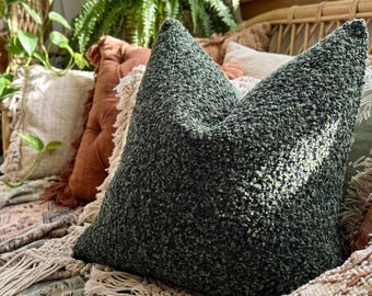 May include: A square throw pillow featuring a dark forest green textured bouclé fabric. The pillow has a dense, nubby surface with a consistent deep green color throughout, showcasing a tactile and looped material construction.