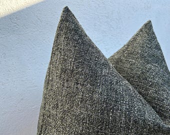 May include: Close-up of two gray decorative throw pillows. The pillows have a textured, woven appearance with a mix of gray and off-white threads. The pillows are angled towards the viewer, showcasing their triangular shape.