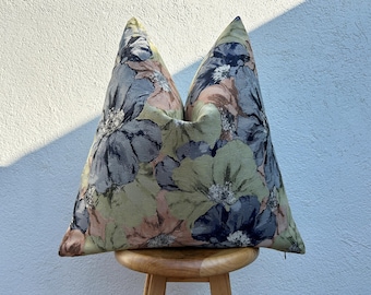 May include: A decorative pillow with a floral pattern. The pillow features large, stylized flowers in shades of blue, green, and peach. The pillow is resting on a small, round wooden stool.