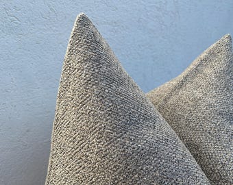May include: Close-up of two textured, gray decorative pillows. The pillows have a woven appearance and are in a neutral color palette. The pillows are likely used for home decor and add a touch of comfort and style to any living space.