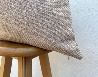 May include: A beige woven pillow with a textured surface rests on a wooden stool. The pillow has a neutral color and a visible zipper. The stool has a light brown finish and a rounded seat.