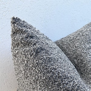 May include: Close-up of two grey decorative throw pillows with a textured, nubby fabric. The pillows are a neutral colour, suitable for various interior design styles. The fabric appears soft and inviting.