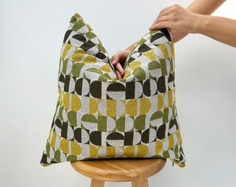 May include: A green, yellow, and white geometric patterned throw pillow with a zipper closure. The pillow is sitting on a wooden stool.