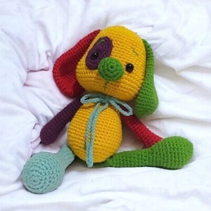 May include: A crocheted stuffed toy dog with yellow, red, green, and purple yarn. The dog has a big, round nose and black eyes.