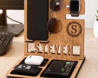 Może przedstawiać: Drewniany organizer na biurko z przegródkami na telefon, okulary, zegarek, portfel, klucze i słuchawki. Organizer jest grawerowany imieniem "STEVEN" i monogramem. Drewno ma naturalne wykończenie.