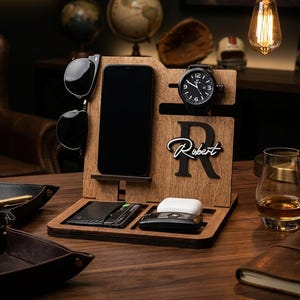Può includere: Organizer da scrivania in legno con fessure per telefono, orologio e occhiali da sole. Presenta un orologio nero, occhiali da sole e un telefono. Include un vassoio per carte e una custodia di ricarica wireless. Personalizzato con il nome "Robert".