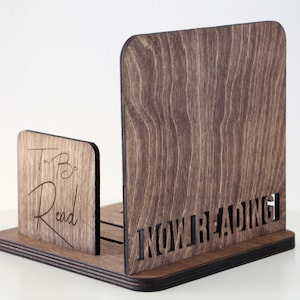 Puede incluir: Soporte de libros de madera con dos compartimentos. El compartimento izquierdo est&aacute; etiquetado como "To Be Read" y el compartimento derecho est&aacute; etiquetado como "Now Reading".