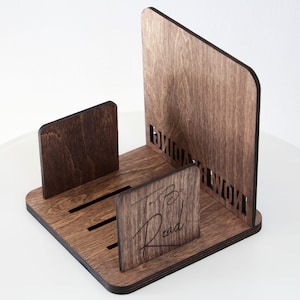 Puede incluir: Un soporte para libros de madera con un tinte marr&oacute;n oscuro. El soporte tiene un dise&ntilde;o recortado que dice "To Be Read" y una ranura para sostener libros.