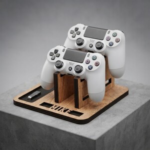 May include: A wooden gaming controller stand featuring two white game controllers resting on vertical supports. The base is made of light-colored wood with dark edges and includes a cutout with the name MIKE and a small rectangular slot for accessories.