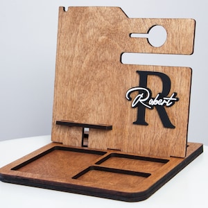 May include: Wooden desk organizer with a phone holder, a small tray, and a cutout for a charging cable. The organizer has a dark brown finish and features the name "Robert" in a cursive font with a large black "R".
