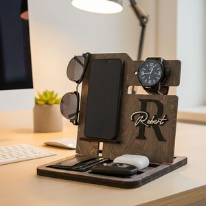 May include: A wooden desk organizer in a dark brown finish. It features slots for a smartphone, sunglasses, and a watch. The organizer also has a tray for small items and the name "Robert" is displayed.