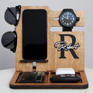 May include: Wooden desk organizer with compartments for a phone, wallet, watch, sunglasses, keys, and wireless earbuds. The organizer has a dark wood finish and features the name "Robert" with a large initial "R".