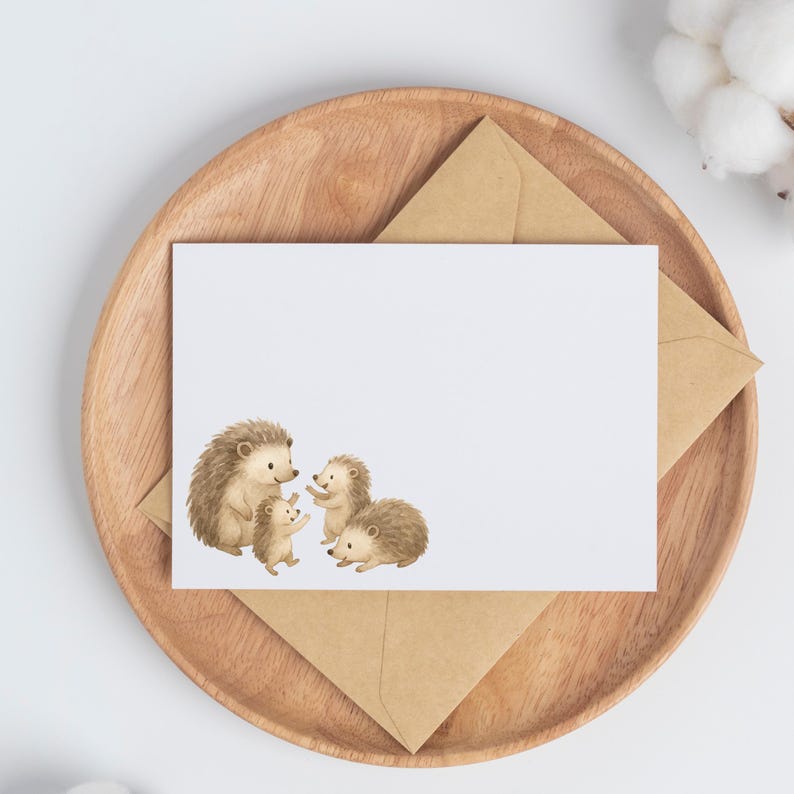 May include: A white card with a watercolor illustration of a family of hedgehogs. The hedgehogs are in shades of brown and tan. The card is on a wooden tray with a brown envelope.