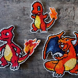 Könnte beinhalten: Drei Aufnäher im Pixel-Art-Stil mit Pokémon-Charakteren. Die Aufnäher zeigen Glumanda, Glutexo und Glurak, jeweils in leuchtenden Orange-, Gelb- und Rottönen mit weißen Umrissen. Der Glurak-Aufnäher hat blaue Flügel.