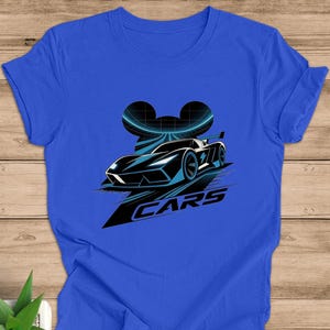 May include: Royal blue t-shirt with a black and blue race car graphic. The design includes a curved shape and the word "CARS" in white. The shirt is made of a soft material.