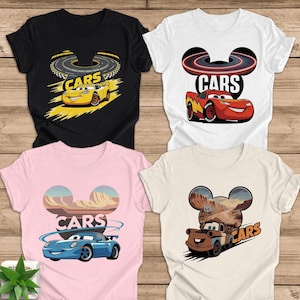 May include: Four t-shirts with "CARS" text and cartoon car designs. The shirts are black, white, pink, and beige. Each shirt features a different car: a yellow race car, a red race car, a blue sports car, and a brown truck.