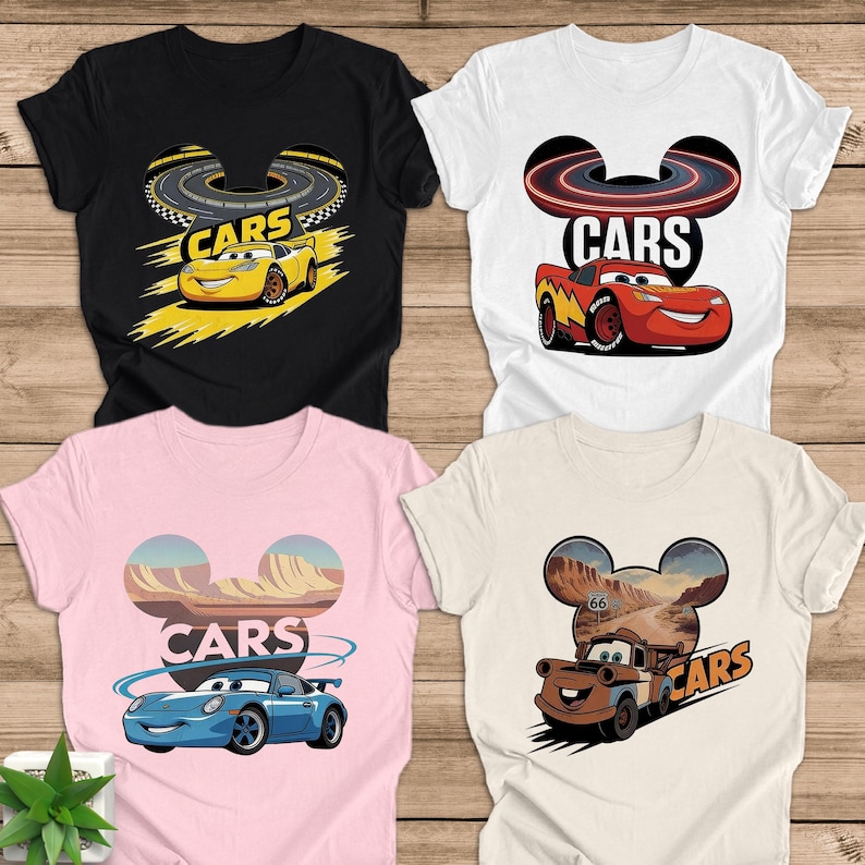 May include: Four t-shirts with "CARS" text and cartoon car designs. The shirts are black, white, pink, and beige. Each shirt features a different car: a yellow race car, a red race car, a blue sports car, and a brown truck.