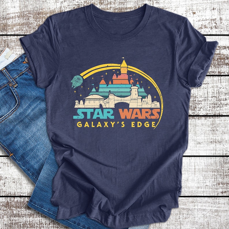 May include: A navy blue t-shirt with a retro-style graphic of a castle with a yellow archway and the text "Star Wars Galaxy's Edge".