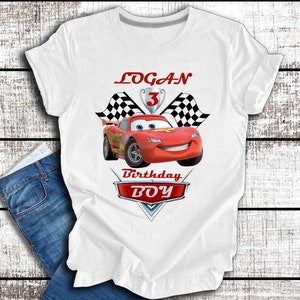 Pu&ograve; includere: Maglietta bianca con un'auto da corsa rossa, bandiere a scacchi e il testo "LOGAN 3 Birthday BOY".