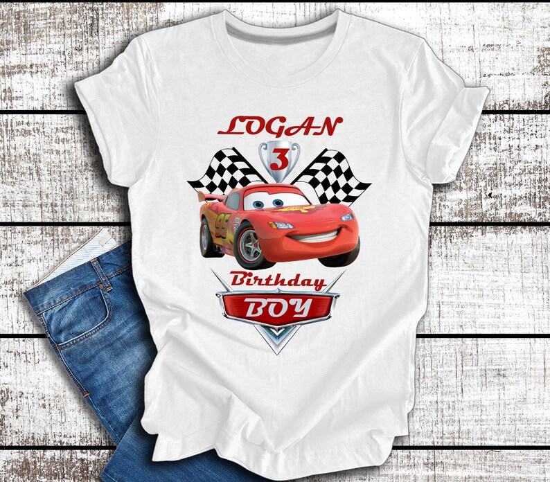 Pu&ograve; includere: Maglietta bianca con un'auto da corsa rossa, bandiere a scacchi e il testo "LOGAN 3 Birthday BOY".