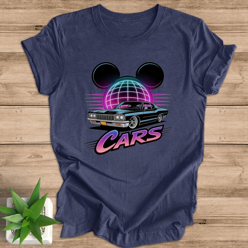 May include: Navy blue t-shirt with a retro design. It features a black car, a geometric globe, and the word "CARS" in a gradient font. The design includes black Mickey Mouse ears above the globe. The shirt is made of soft material.