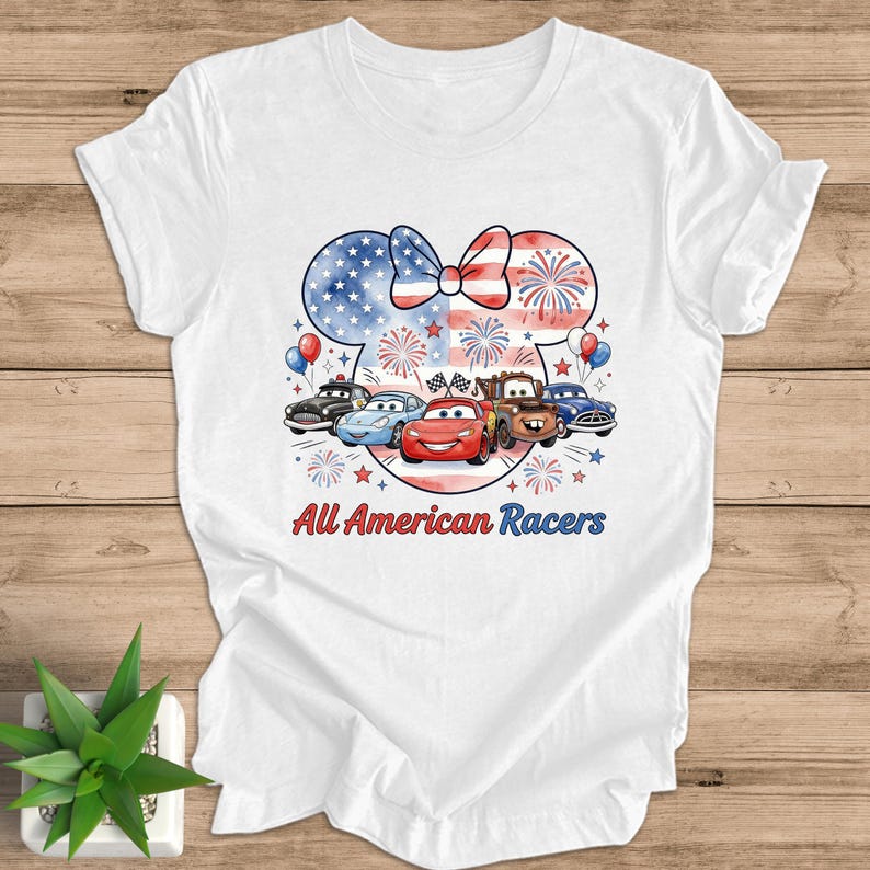 May include: White t-shirt featuring a graphic of cartoon cars with a patriotic theme. The design includes a bow and mouse ears filled with the American flag, fireworks, and the text "All American Racers".