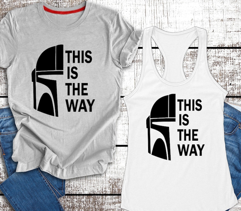 May include: Two shirts featuring a black and white graphic of a Mandalorian helmet and the text "This is the way". One shirt is a grey t-shirt and the other is a white tank top.