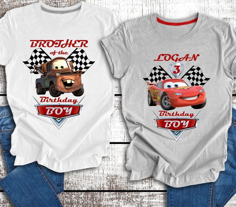Pu&ograve; includere: Due magliette bianche a tema Cars. La maglietta a sinistra presenta Mater di Cars con il testo "Brother of the Birthday Boy". La maglietta a destra presenta Saetta McQueen con il testo "LOGAN Birthday Boy".