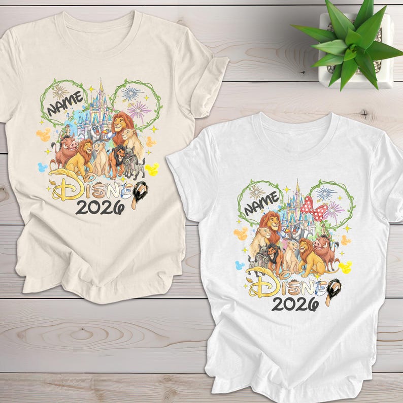 May include: Two t-shirts, one cream and one white, featuring a Disney-themed design. The design includes characters from The Lion King, a castle, and the text "Disney 2026". A green Mickey Mouse-shaped wreath surrounds the word "Name".