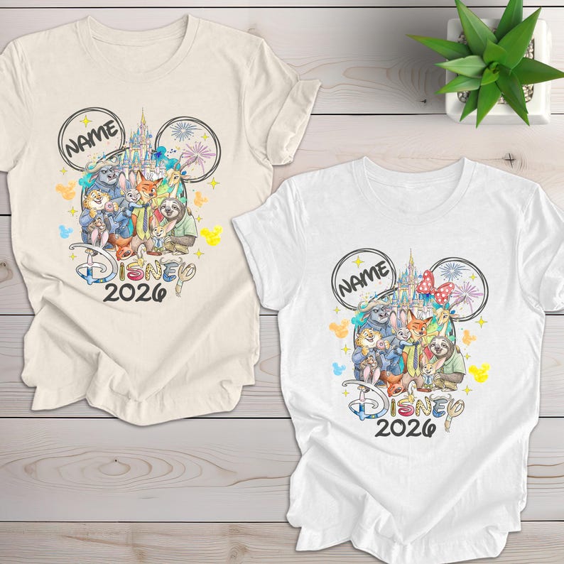 May include: Two t-shirts, one cream and one white, featuring a Disney-themed design. The design includes Disney characters, a castle, fireworks, and the text "Disney 2026". Each shirt has a space for a name.