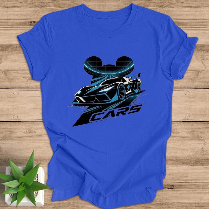 May include: Royal blue t-shirt with a black and blue race car graphic. The design includes a curved shape and the word "CARS" in white. The shirt is made of a soft material.