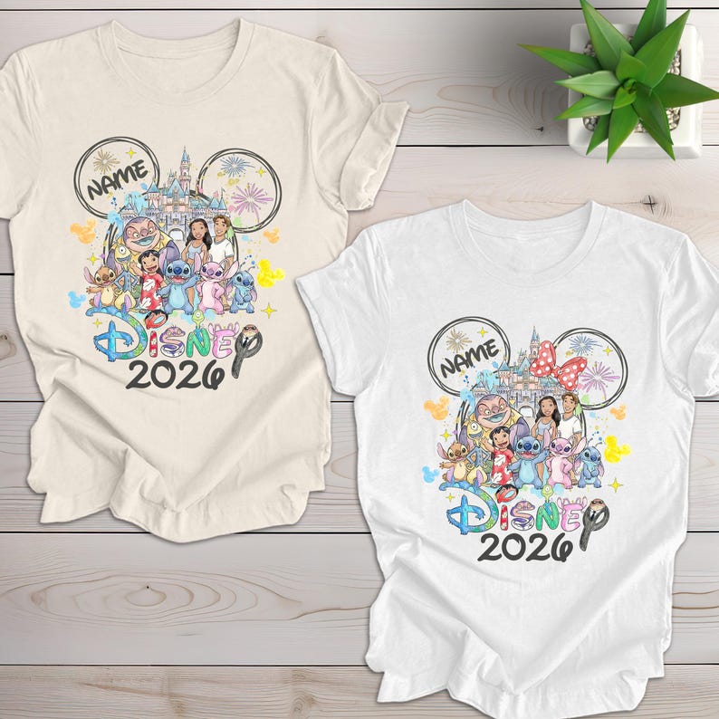 May include: Two t-shirts, one cream and one white, featuring a colorful Disney design. The design includes Disney characters, a castle, fireworks, and the text "Disney 2026". A name is written inside a Mickey Mouse ear.