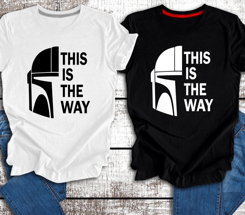 May include: Two t-shirts featuring a black and white image of a Mandalorian helmet and the text "This is the way". One t-shirt is white with black text and the other is black with white text.