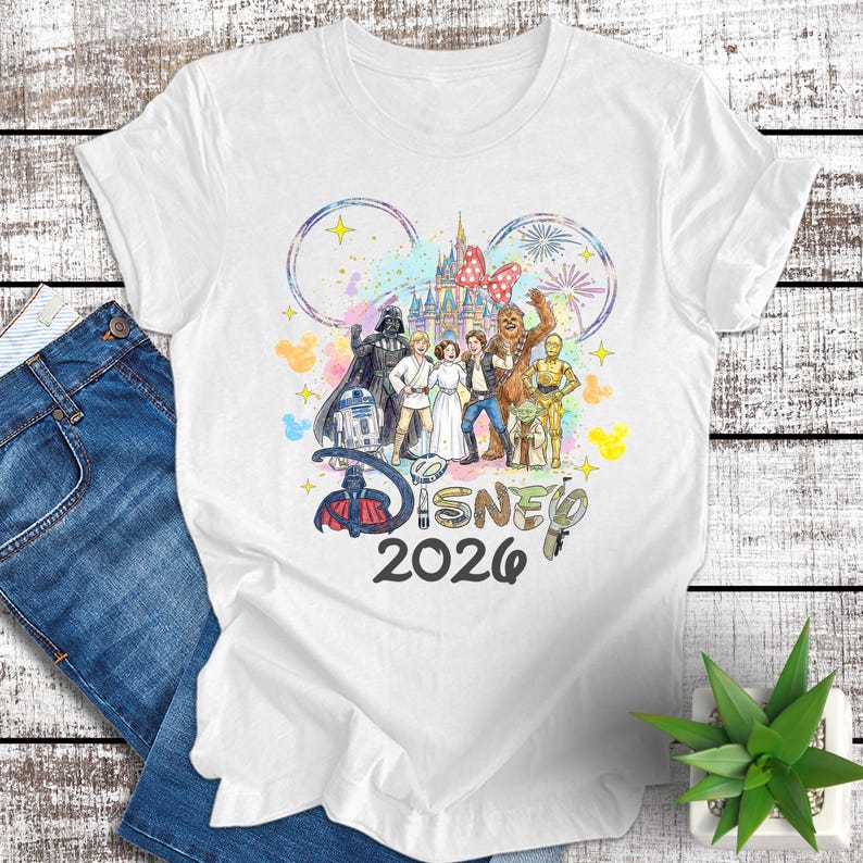 May include: White t-shirt featuring a colorful Disney and Star Wars graphic. The design includes iconic characters, the Disney logo, and the text "2026". The shirt is made of a soft material.