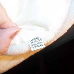 Puede incluir: Tela de piel blanca con una etiqueta de cuidado blanca que dice "Clean by Fur Method Do Not Brush Press or Steam".