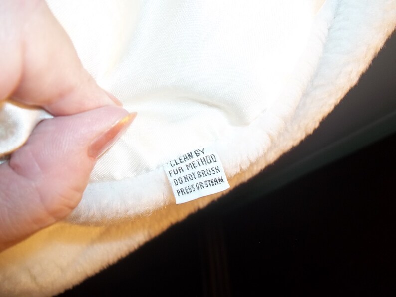 Puede incluir: Tela de piel blanca con una etiqueta de cuidado blanca que dice "Clean by Fur Method Do Not Brush Press or Steam".