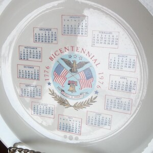 May include: A white ceramic plate featuring a calendar design for the year 1976, commemorating the Bicentennial. The design includes the American flag, an eagle, and the words "Bicentennial 1776-1976".