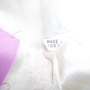 Puede incluir: Una etiqueta de tela blanca con el texto "MADE IN U.S.A." impreso en ella. La etiqueta est&aacute; unida a una prenda blanca.
