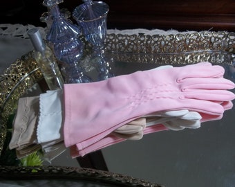 May include: A stack of pink, white, and beige gloves with a delicate lace trim. The gloves are folded and arranged on a silver tray with a gold ornate border.