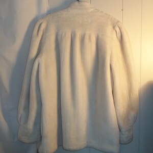 Puede incluir: Una chaqueta de piel sint&eacute;tica blanca con mangas largas y cuello alto.