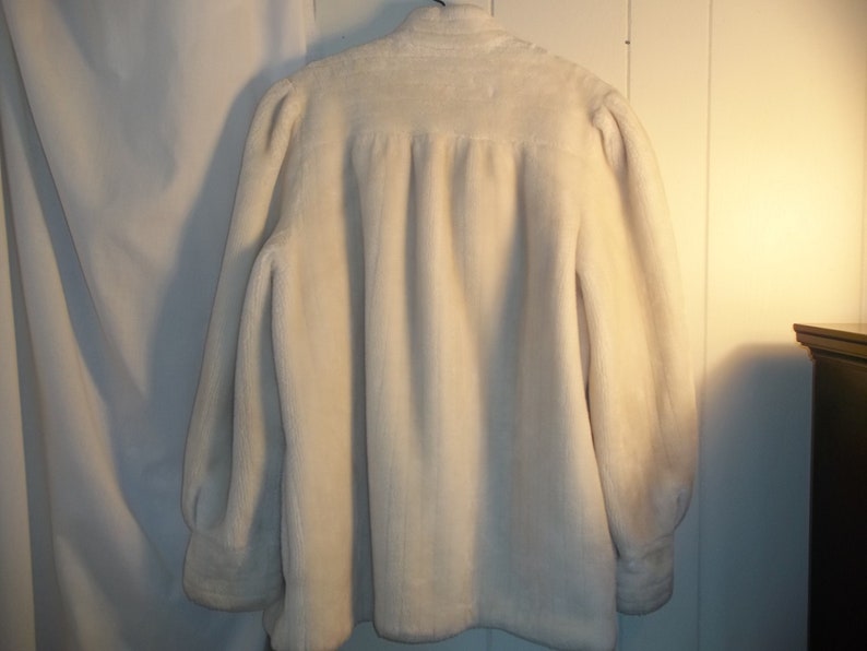 Puede incluir: Una chaqueta de piel sint&eacute;tica blanca con mangas largas y cuello alto.