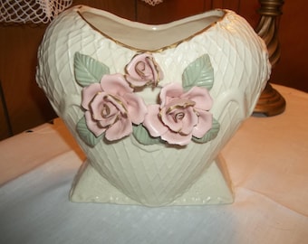 Puede incluir: Un jarrón de cerámica blanco en forma de corazón con un borde dorado y tres rosas rosas con detalles dorados.