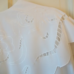 May include: White cotton fabric with a delicate floral embroidery design. The fabric has a scalloped edge and is perfect for a tablecloth or a decorative piece.