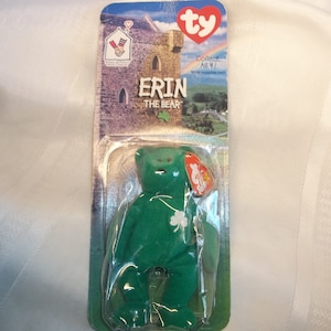 May include: A green Ty Beanie Baby plush toy named "Erin the Bear" in its original packaging. The packaging features a cartoon image of a castle and the Ty logo.