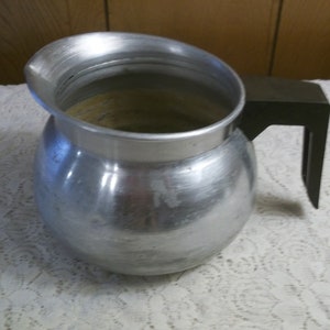 May include: A silver aluminum pitcher with a black plastic handle. The pitcher has a round body and a wide mouth.