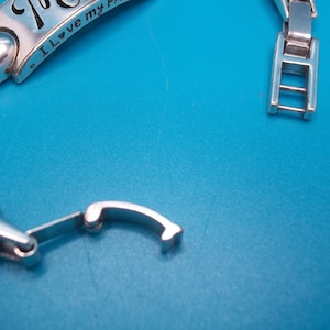 May include: Silver bracelet with a clasp and a decorative charm. The charm has the inscription "I love my..." and a small heart. The bracelet is on a blue background.