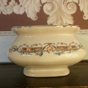 May include: A cream-colored ceramic sugar bowl with a scalloped rim and a floral design in shades of pink, blue, and green.