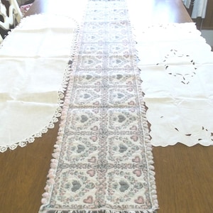 May include: Three white table runners with lace trim. The center runner has a pink and gray floral pattern with hearts.